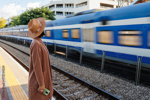 Girl at the railway station. A young woman in a coat and hat stands on the station platform and looks at the train.