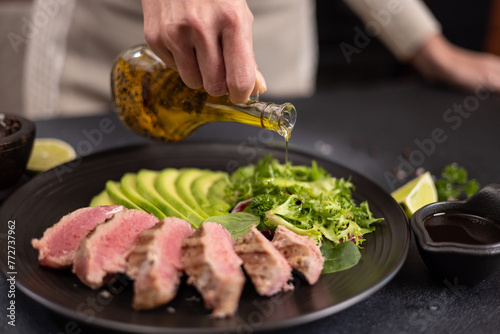 Woman pours cooking olive oil on a salad on a plate with grilled cooked piece of tuna fillet © Anatoly Repin