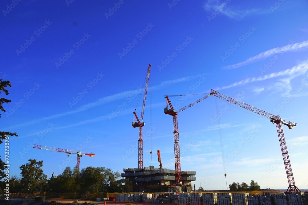 Red tower cranes in a construction site against a blue sky