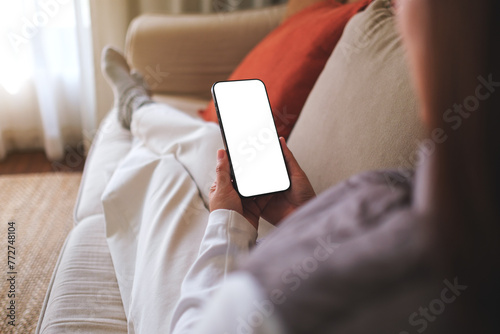 Mockup image of a woman holding mobile phone with blank desktop white screen while sitting on a sofa at home © Farknot Architect