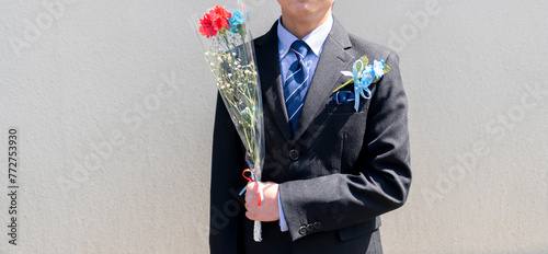 花束を持ったスーツ服装の少年。小学生の卒業式。卒業式の記念ギフト、コサージュ。イベント。子どもの成長。