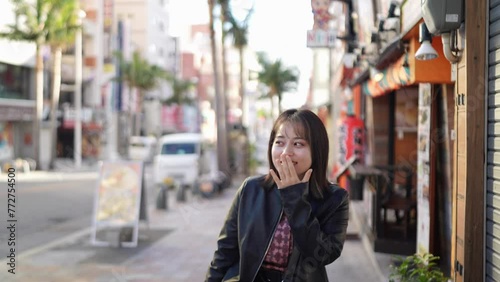 Slow-motion video of an Okinawan woman in her 20s in winter clothes walking on Kokusai Street in Naha City, Okinawa Prefecture with a smile 沖縄県那覇市の国際通りを笑顔で歩く冬服の20代の沖縄県民女性のスローモーション映像 photo