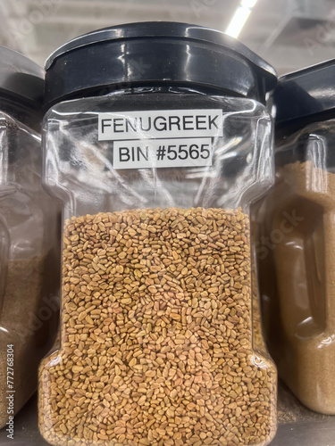 A close up, slightly lower than eye level view, of a container of Fenugreek in a bulk section of the supermarket