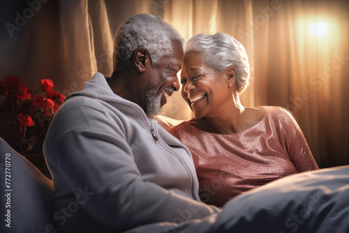 An elderly dark-skinned man and woman sitting side by side on a bed, showing love and affection towards each other