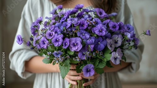  A close-up of a person holding a bouquet of flowers, with purple flowers at the center and green leaves surrounding it