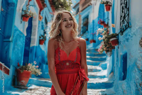 A young woman with a red dress visiting the blue city Chefchaouen, Morocco. A happy tourist walking in a Moroccan city street