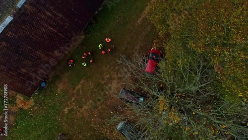 Aerial shot of people in the forest with fluorescent vests and cars parked on the road.
