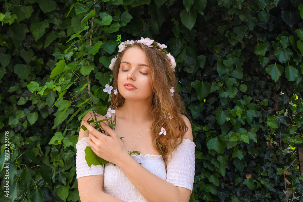 Beautiful young woman with flowers in her hair near green ivy outdoors. Summer solstice Beautiful young woman with flowers in her hair near green ivy outdoors. Summer solstice