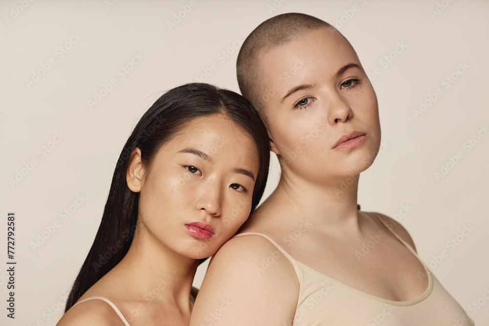 Medium closeup studio portrait of two diverse young Asian and Caucasian female friends wearing neutral toned bras posing for camera Medium closeup studio portrait of two diverse young Asian and Caucasian female friends wearing neutral toned bras posing for camera