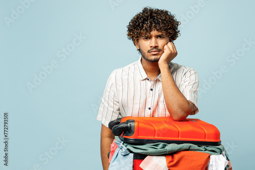 Traveler sad Indian man wear white casual clothes hold suitcase bag prepare isolated on plain blue background. Tourist travel abroad in free spare time rest getaway. Air flight trip journey concept. photo