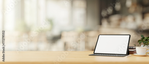 A tablet mockup with a wireless keyboard on a wooden table in a cosy, minimalist coffee shop.