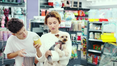 Interested woman accompanied by teenage son meticulously selecting quality dog food for beloved Yorkshire terrier in pet store, attentively examining packaging and considering choice