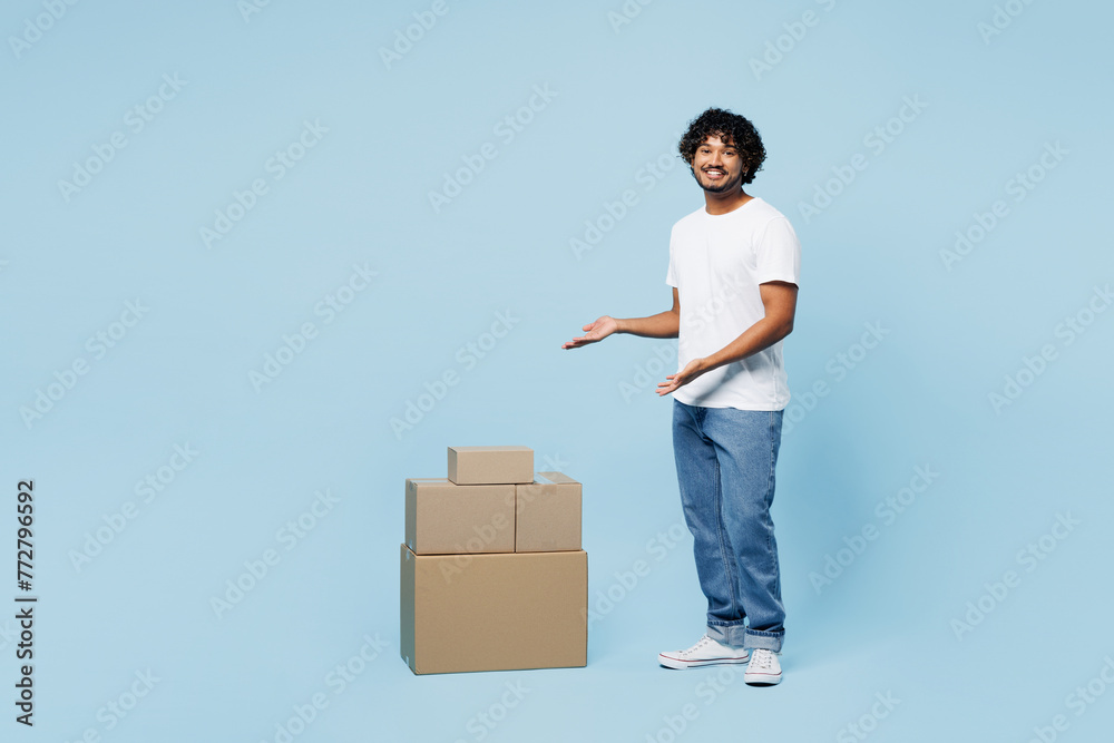 Full body side view young happy Indian man wear white t-shirt casual clothes point on stack cardboard blank boxes isolated on plain pastel light blue cyan background studio portrait Lifestyle concept - obrazy, fototapety, plakaty 