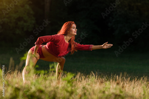 Fitness woman doing stretching exercises during outdoor cross training workout, Fiery-haired girl engages in workout amidst park's woodland setting.