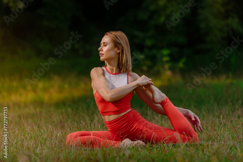 Sporty girl during yoga workout at nature stretching her legs. Tranquil stretch: Alone in summer park, woman finds serenity stretching back and legs.