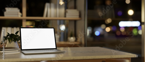 A white-screen laptop computer mockup on a desk in a modern home office at night. © bongkarn