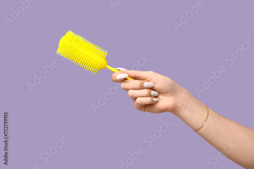 Female hand with yellow hair brush on lilac background