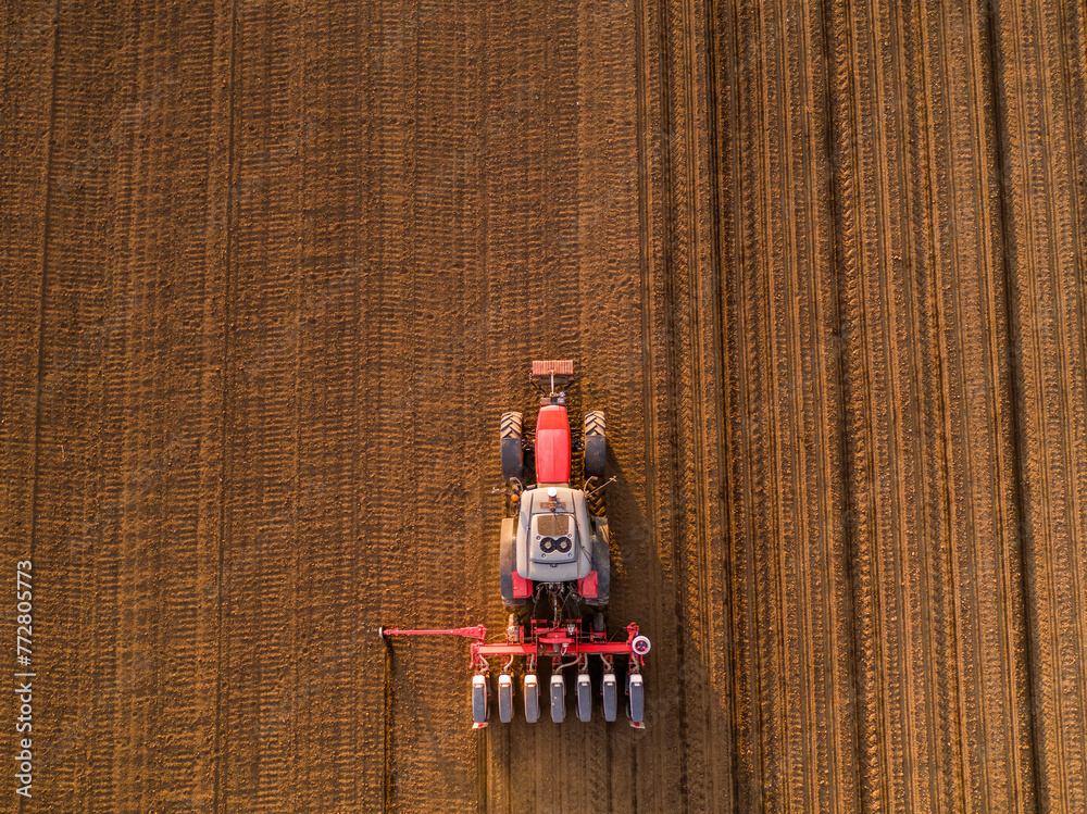 Aerial shot of a farmer seeding, sowing crops at field. Sowing is the process of planting seeds in the ground as part of the early spring time agricultural activities. - obrazy, fototapety, plakaty 
