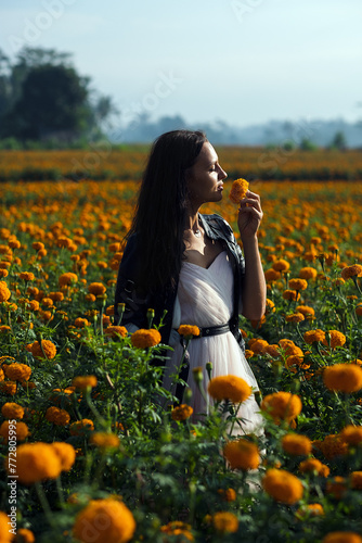 A young girl, brunette, walks through a field strewn with orange flowers and enjoys life.