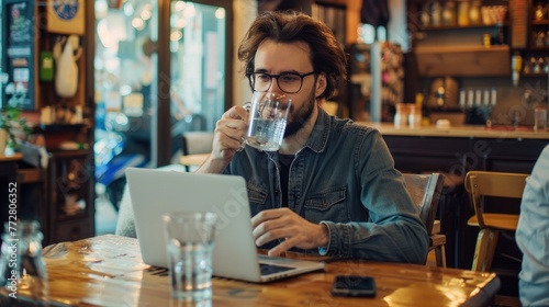 Freelancer drinking water sitting at table with laptop on cafe.
