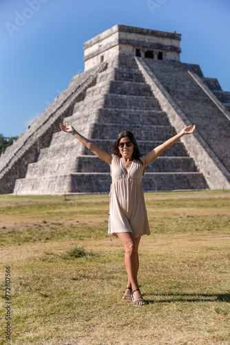 Young female tourist posing in front of the Chichen Itza pyramid with her arms stretched upwards happy to visit one of the seven wonders of the world.