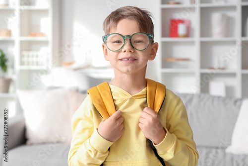 Cute little boy in eyeglasses with schoolbag at home, closeup