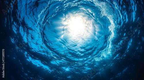 View from underwater looking up at the swirling water's surface with sunlight piercing through