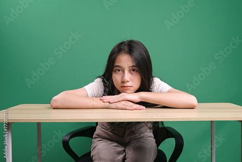 Young beautiful woman looking tired and bored with heads on table against green background