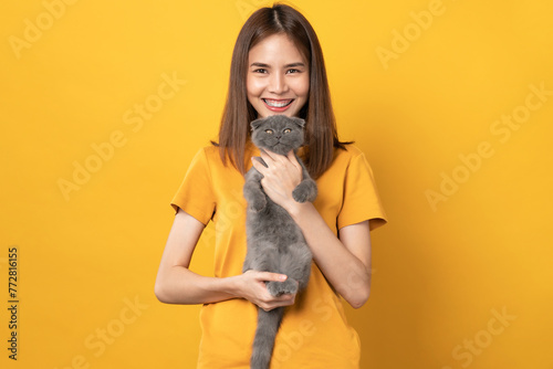 Studio shot of cheerful beautiful Asian woman hands holding a small blue-black kitten of the Scottish fold breed on orange background.