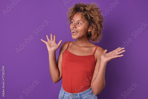 Young overjoyed African American woman teen spreads arms to sides seeing friend and rejoicing at long-awaited meeting after separation on summer vacation stands in purple studio. Schoolgirl, student