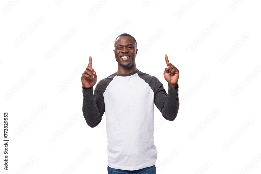 Naklejka premium young joyful african guy dressed in a black and white sweatshirt and jeans on a white background with copy space