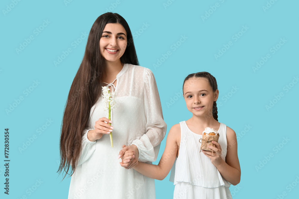 Happy smiling young woman and her daughter with Easter cake and flower on blue background