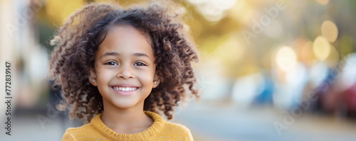 Smiling little African American child on blurry street background portrait. Cute immigrant offspring walks in city. Black kinky haired girl. photo