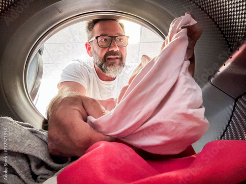 Man Doing Laundry Reaching Inside Washing Machine. One adult male washing clothes. View from inside the laundry. Homework husband. People using washing machine in laudromat