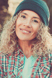 Middle age beautiful woman portrait with hipster style and warm woolen hat in outdoor with defocused bokeh nature background - cheerful happy people female caucasian looking at camera