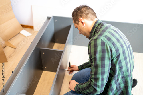 Furniture assembly. The furniture assembler takes a white shelf, tightens the screw with a hex wrench. Collector of furniture. Moving concept, furniture assembler, self assembly