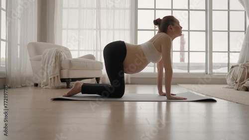 Young pregnant woman doing yoga at home. Pregnant girl with big belly practice yoga, does stretching, deep breath after wake up, meditation. Healthy pregnant yoga, prenatal active workout concept. photo