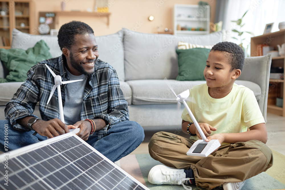 Portrait of smiling African American father and son holding wind turbine model with renewable energy sources - obrazy, fototapety, plakaty 
