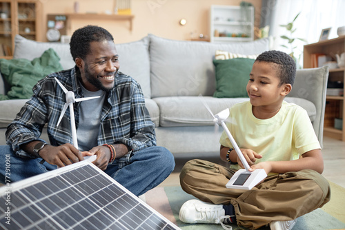 Portrait of smiling African American father and son holding wind turbine model with renewable energy sources photo