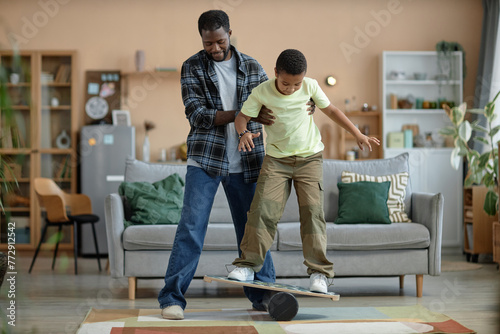 Full length portrait of African American father teaching son standing on balance board