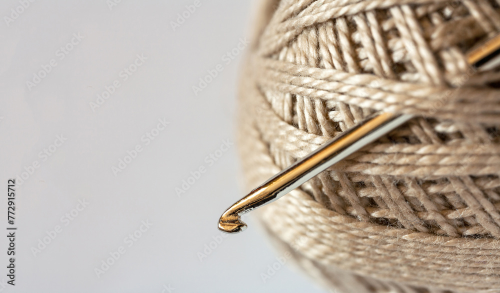Close-up on a skein of natural beige cotton yarn and a metal crochet hook. Empty space for text on the left on a white background. DIY concept. Flat lay, copy space, macro