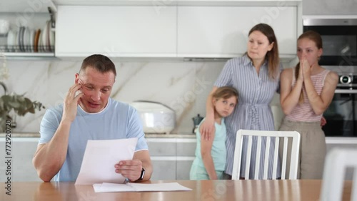 Family quarrel at home kitchen in presence of children. Middle-aged man reads, studies financial document and wife scolds him for signing unreasonable unprofitable contract with bank, lender photo