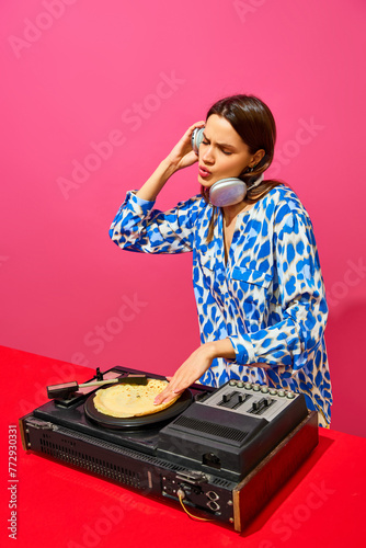 Young stylish woman, dj using sound mixer with pancake instead of vinyl record on pink background. Creative music poster. Party. Concept of food pop art photography, creativity, quirky style