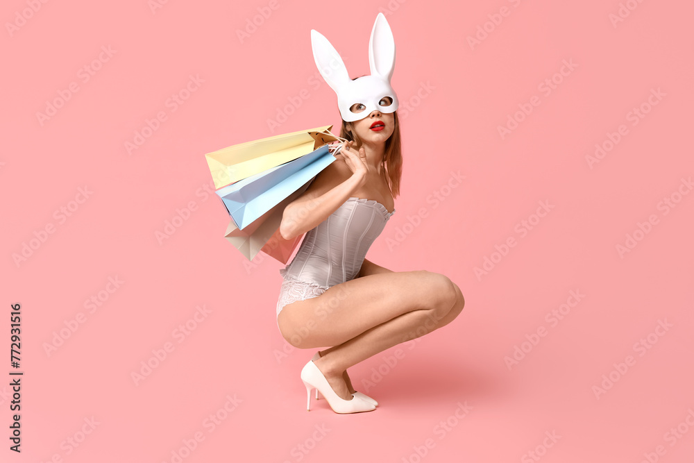 Sexy young woman in bunny mask with shopping bags sitting on pink background. Easter celebration Sexy young woman in bunny mask with shopping bags sitting on pink background. Easter celebration