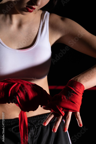 The athlete wraps her hands with a boxing bandage. Preparation for an important fight. The woman focused during the last steps before going to the ring. © fotodrobik