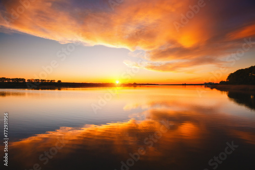 Attractive view of the sunset over the calm surface of the water. © Leonid Tit