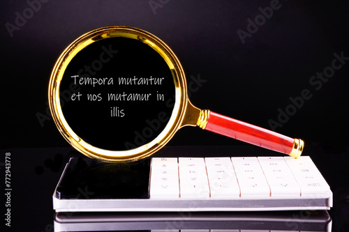 Tempora mutantur et nos mutamur in illis Translated from Latin, it means Times are changing, and we are changing with them. through a magnifying glass on a black background in white font photo