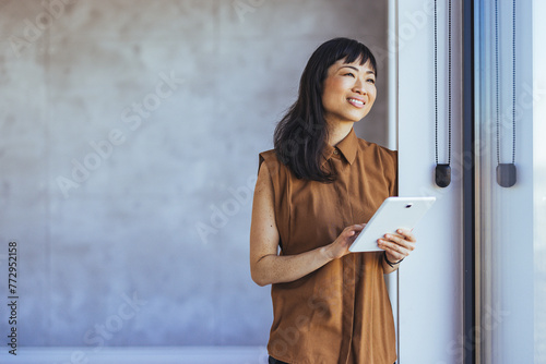 Portrait of young businesswoman standing in office with a digital tablet. Confident asian businesswoman in office. Portrait of young business woman in modenr co-working space photo