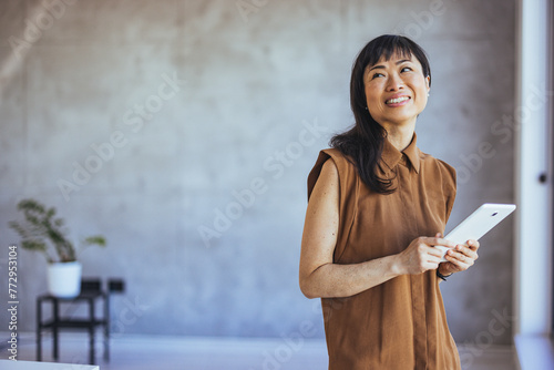 Portrait of young businesswoman standing in office with a digital tablet. Confident asian businesswoman in office. Portrait of young business woman in modenr co-working space photo