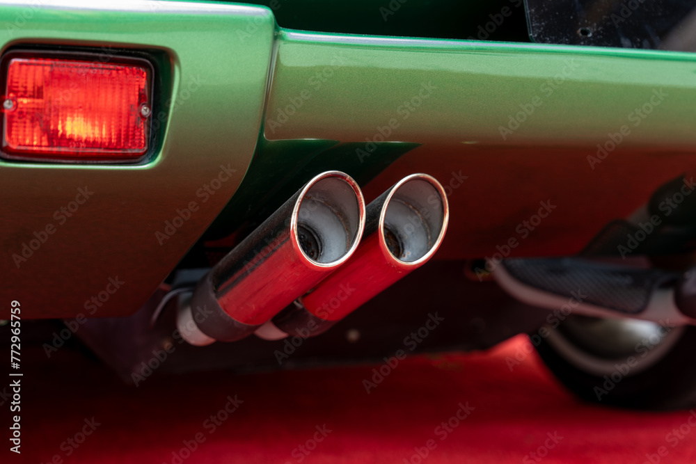 Cropped of double exhaust pipe and back part with tail light of modern green parked car. Waste gases release system of sports auto of new generation